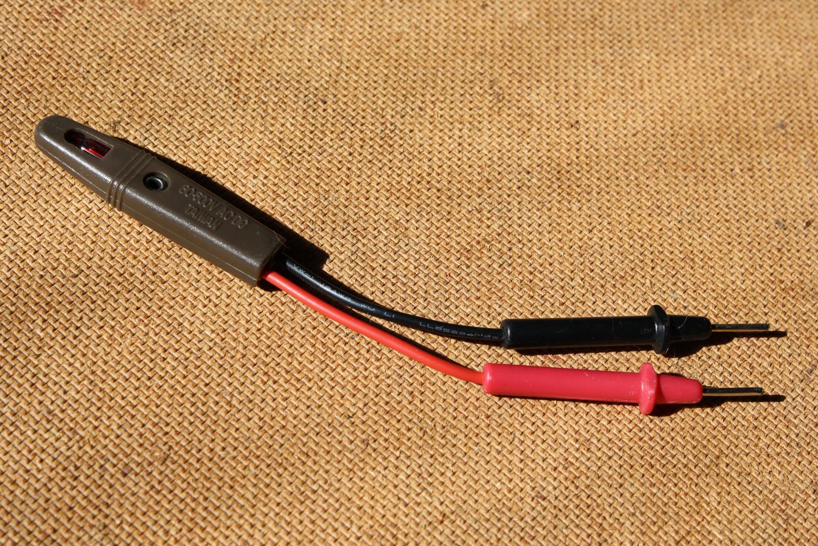 Electrical voltage tester and red and black probes resting on fabric